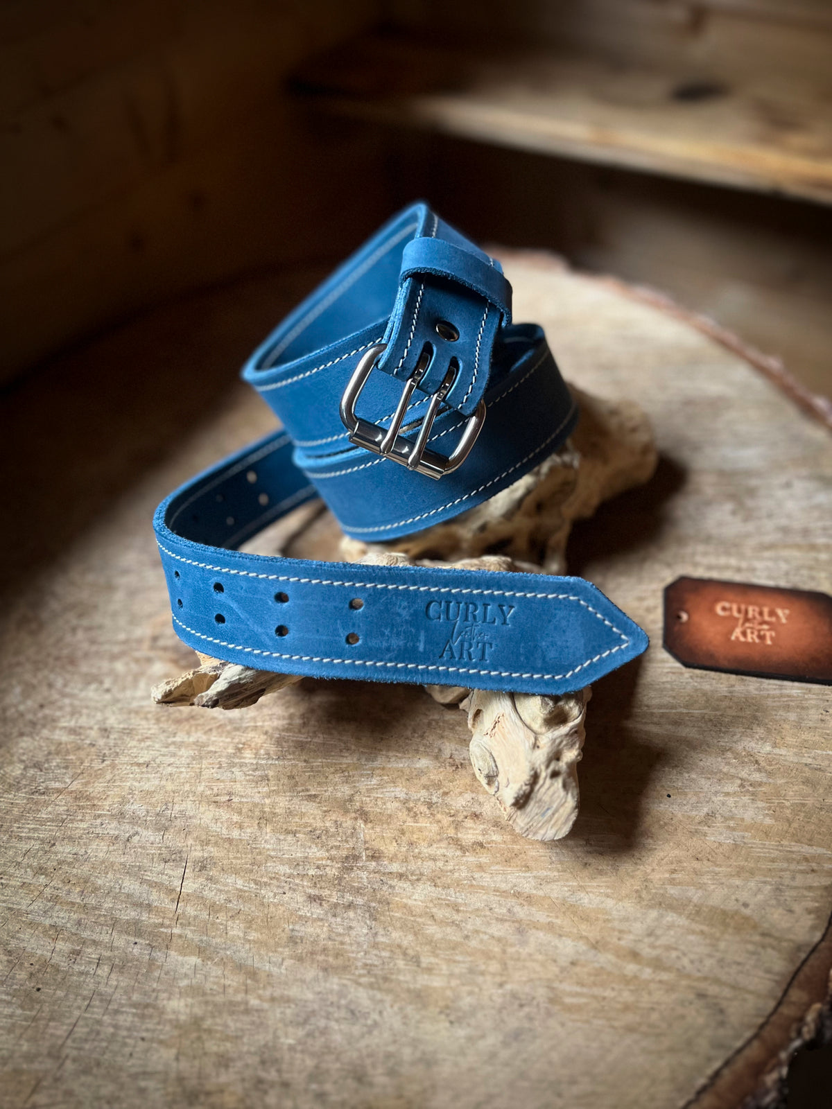 Blauer Ledergürtel mit Doppeldornschnalle, hellen Nähten und geprägtem Curly Leather Art Logo