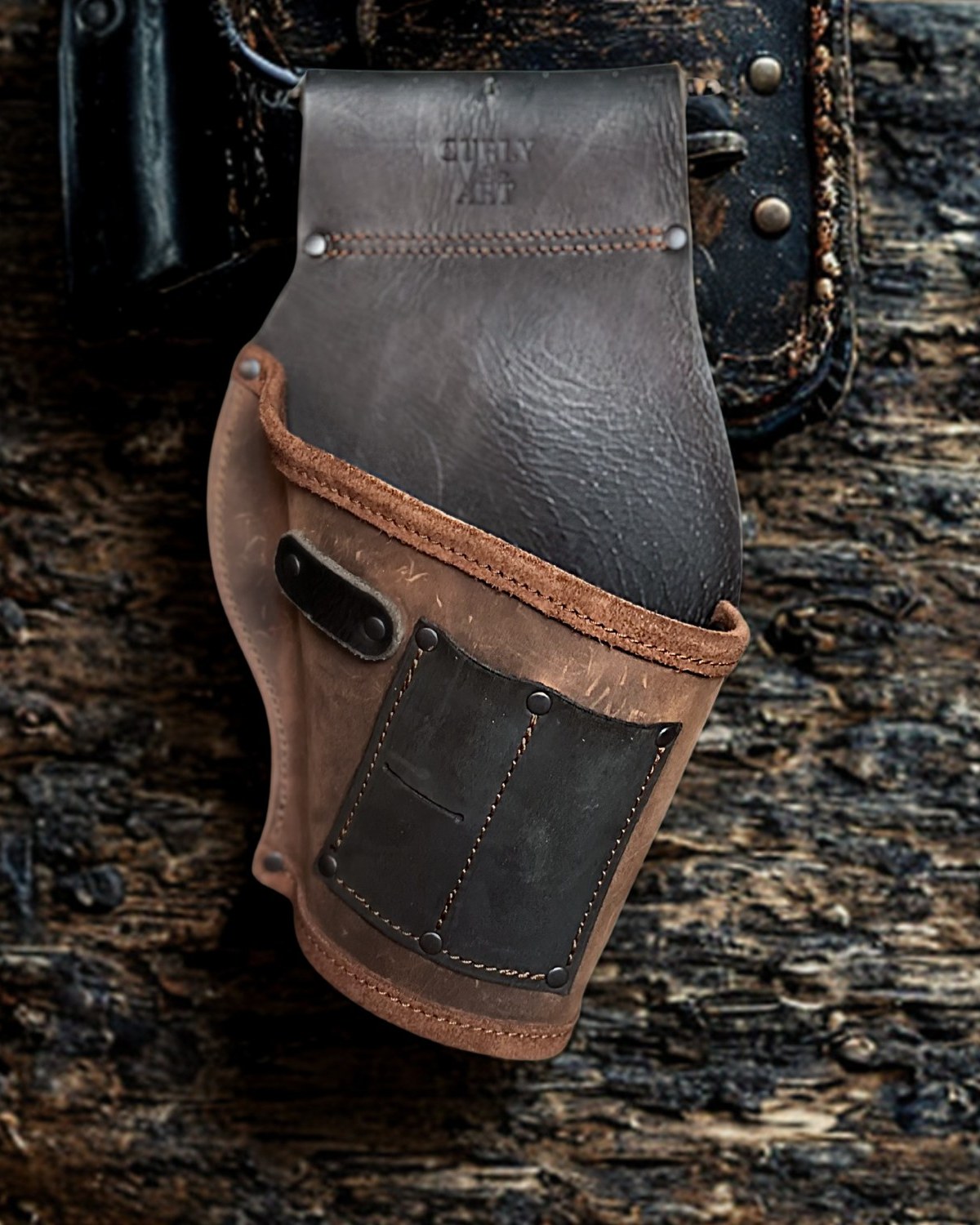 Braun-schwarzer Akkuschrauberhalter aus Leder mit zwei kleinen Frontfächern und einer seitlichen Schlaufe vor rustikalem Holz