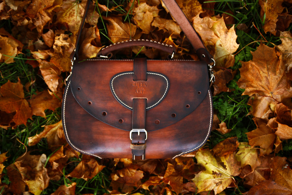 Braune Leder-Umhängetasche Skadi mit Schultergurt auf gelbem und orangefarbenem Herbstlaub.