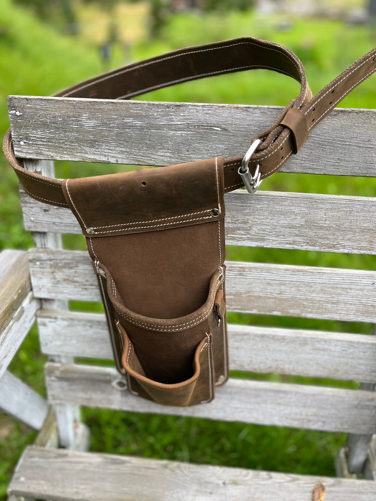 Braune Schraubentasche aus Leder mit Hauptfach, Fronttasche und D-Ring an einem Ledergürtel auf einer hellen Holzbank