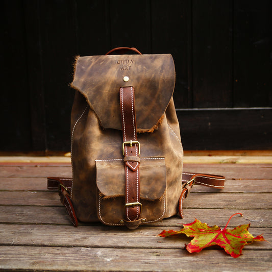 Brauner Lederrucksack mit wilder Klappe aus natürlicher Lederkante auf einer Holzfläche mit Herbstblättern