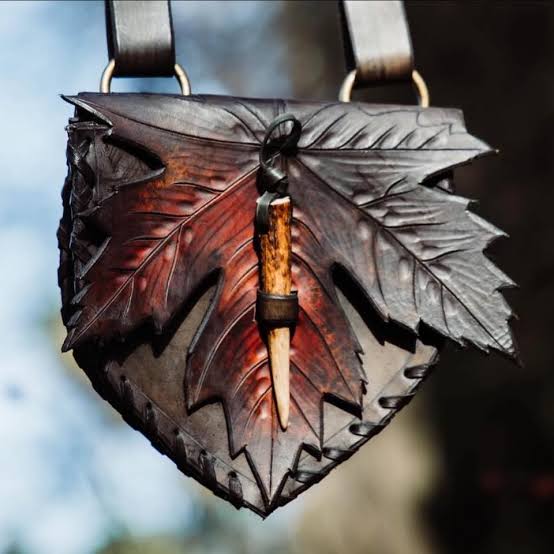 Dunkle Ahornblatt Ledertasche mit rötlichen Farbakzenten und hellem Knebelverschluss.