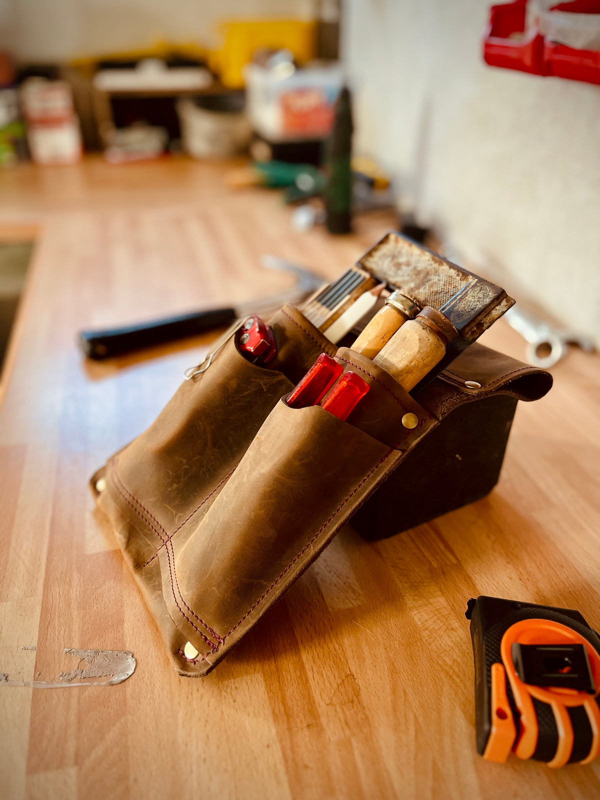 Gefüllte braune Leder-Werkzeugtasche mit sichtbaren Nähten und Nieten auf einer Werkbank