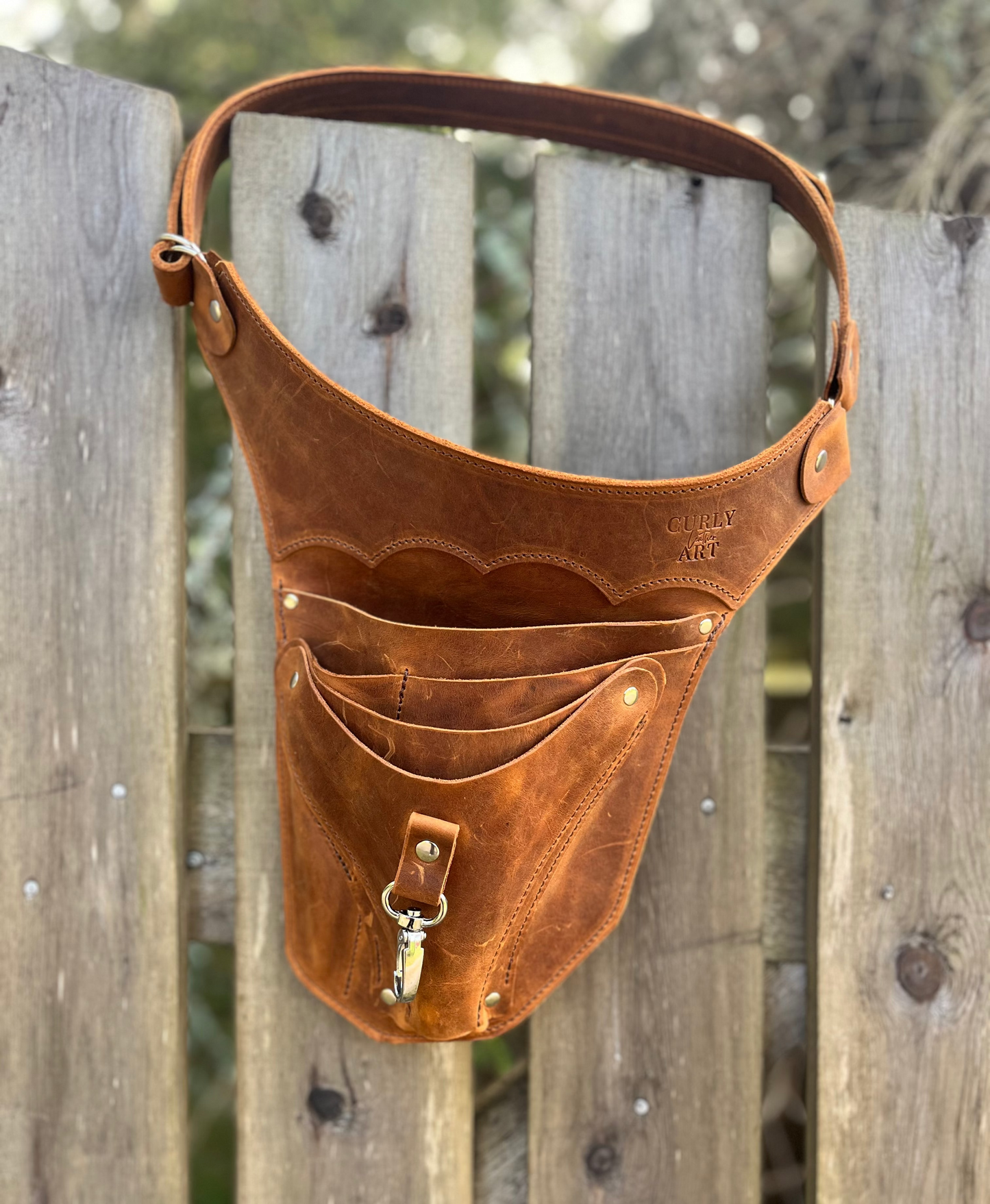 Großer brauner Gartenwerkzeuggürtel aus Leder mit fünf Fächern und Karabiner am Holzzaun
