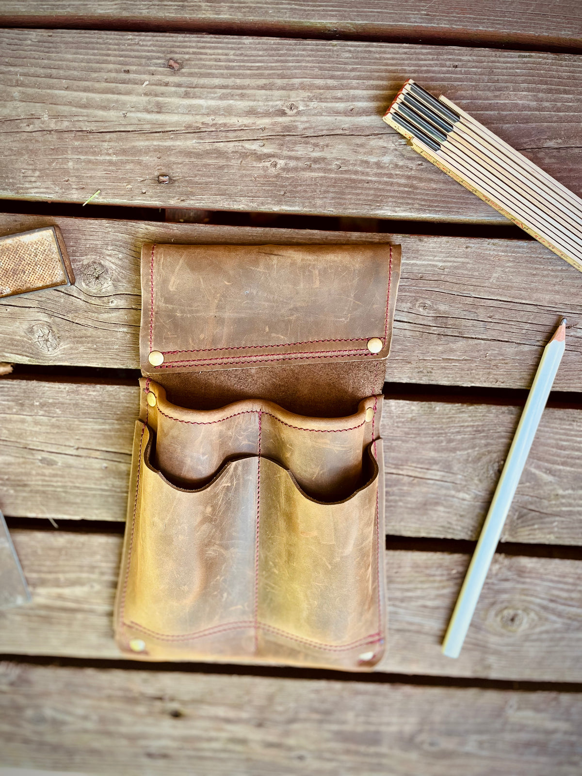 Leere braune Leder-Werkzeugtasche mit vier offenen Fächern auf einer Holzbank