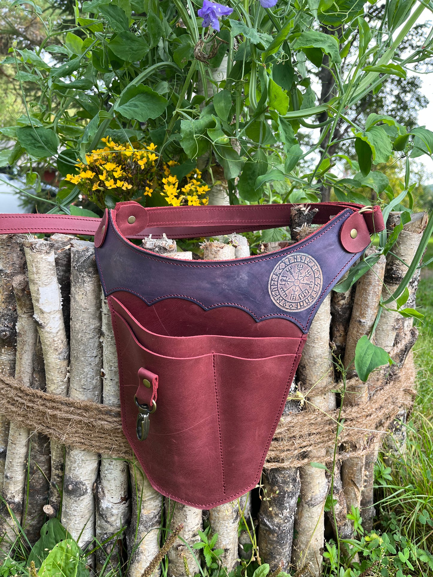 Weinroter Leder-Gartengürtel mit violettem Vegvísir-Kranz an einem Birkenholzzaun