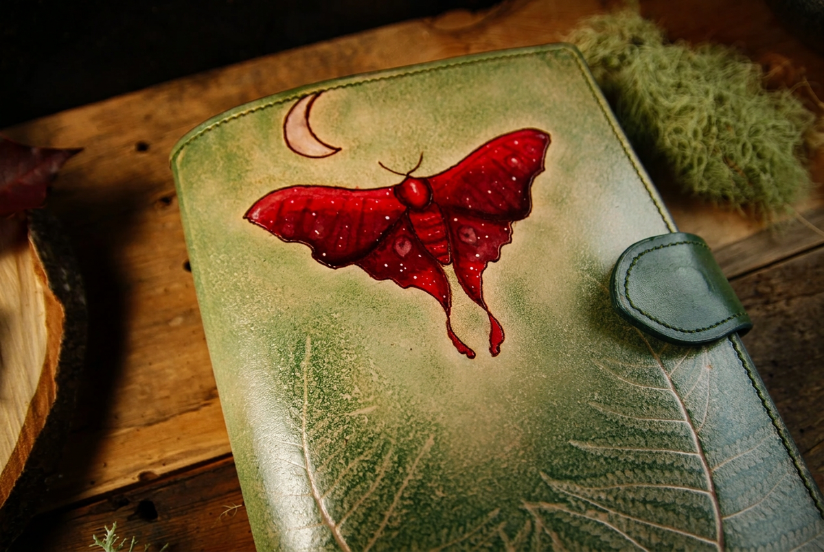 Nahansicht der Leder-Notizbuchhülle mit roter Motte, Farnmotiv und grüner Verschlusslasche